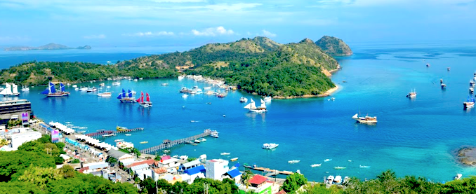 A captivating view of Labuan Bajo, a thriving coastal town located on the western edge of Flores Island, Indonesia. This image showcases the charming harbor, dotted with boats and liveaboards, poised to embark on island explorations. Surrounded by lush hills, the waterfront glows under the radiant colors of a tropical sunset, reflecting off the calm waters. As the entrance to Komodo National Park, Labuan Bajo serves as a vibrant hub for adventure, tourism, and cultural experiences, drawing travelers from around the world to its natural beauty and scenic landscapes.